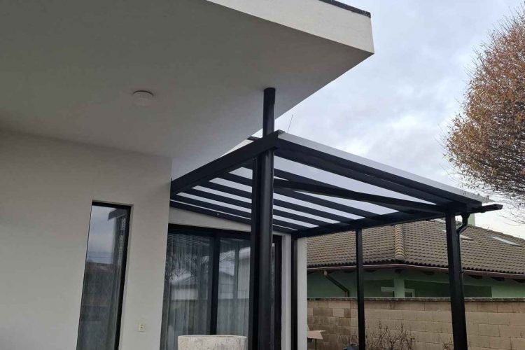 Pergola na terasu s čiernou hliníkovou konštrukciou a polykarbonátovou strechou napojená na rodinný dom, hormax